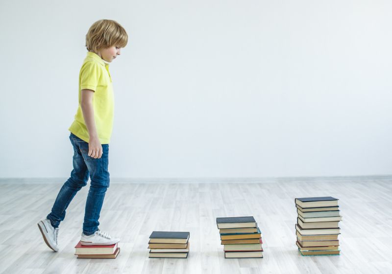 Un niño que subiendo escalones que están hechos por pilas de libros. Imagen que representa el programa educativo AprendEmos.