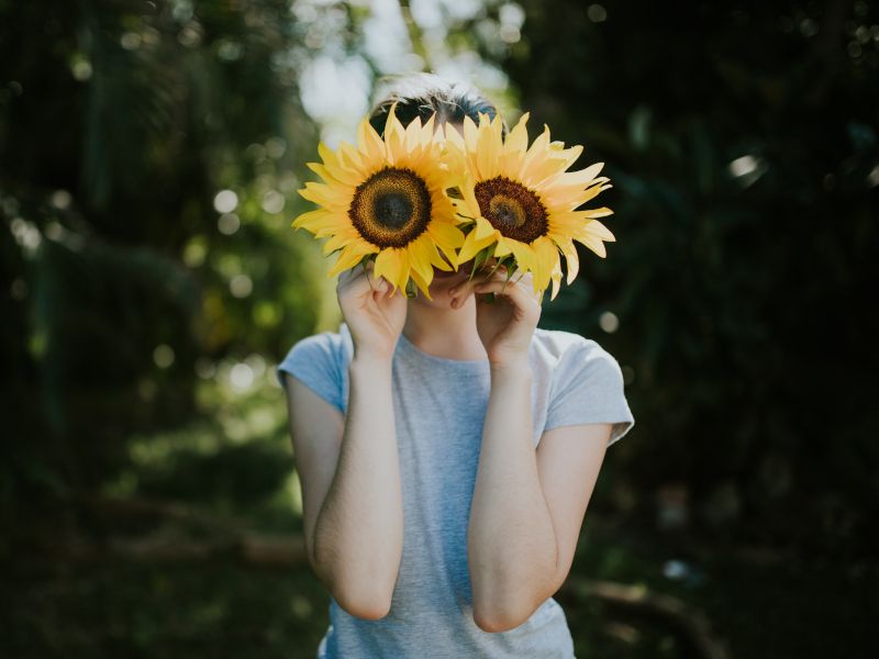 Una Chica con dos flores gigantes tapando la cara.